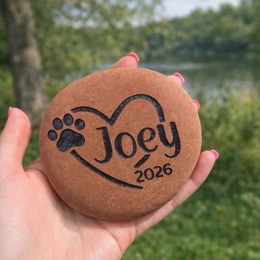 Person holding a engraved stone with 'Joey 2026' in a natural setting