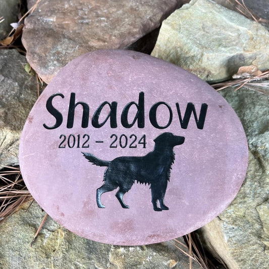 Pink stone with 'Shadow' and a dog silhouette engraved, set against a natural stone background.